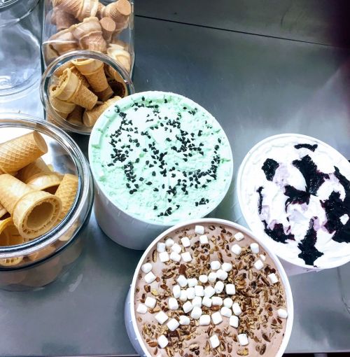 A variety of ice cream tubs in different flavors, with ice cream cones in jars nearby.