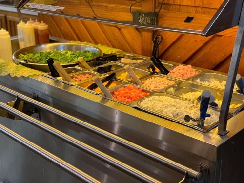 A salad bar with various toppings, including lettuce, diced tomatoes, and shredded cheese, in metal trays.