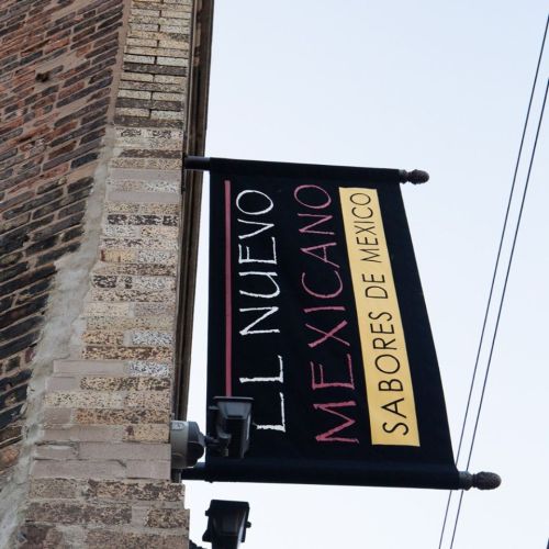 Sign for "El Nuevo Mexicano" featuring the tagline "Sabores de Mexico," hanging from a brick building.