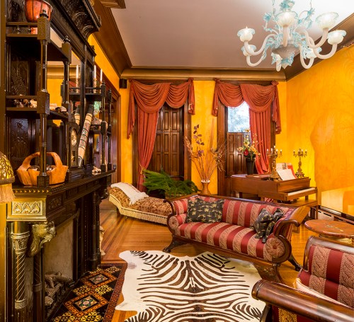 A cozy living room with yellow walls, ornate furniture, a zebra-patterned rug, and a grand piano in the background.