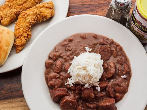 A plate of rice topped with beans and sausage, accompanied by fried chicken tenders and a biscuit.