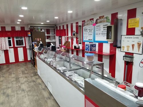 Interior of an ice cream shop with red and white striped walls, display freezers, and a menu board.
