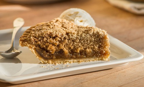 A slice of pie with a crumbly topping, served on a plate with a scoop of ice cream beside it.