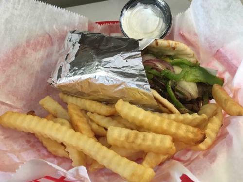 A foil-wrapped sandwich with grilled vegetables and a side of crinkle-cut fries, served in a red basket.