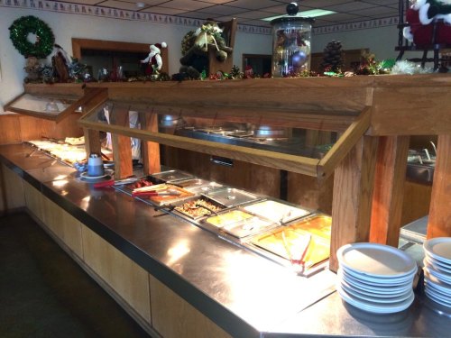 A buffet setup with food trays under glass covers, wooden counters, and holiday decorations in a cozy dining area.