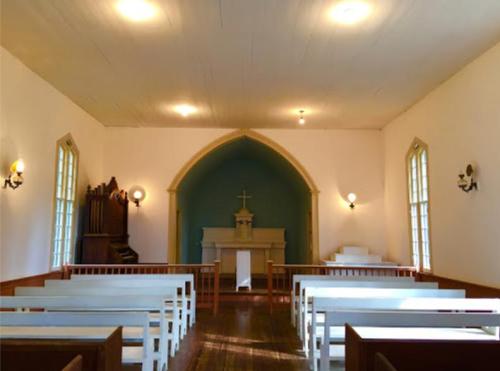 Interior of a simple church with white pews, a blue wall behind the altar, and an organ in the corner.
