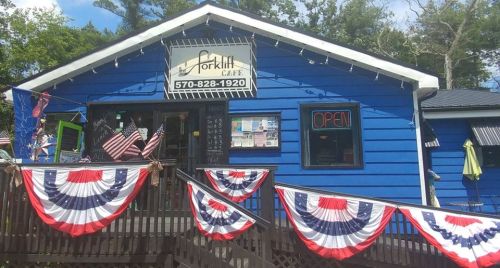 A blue café building decorated with red, white, and blue bunting, featuring an "Open" sign and outdoor seating.