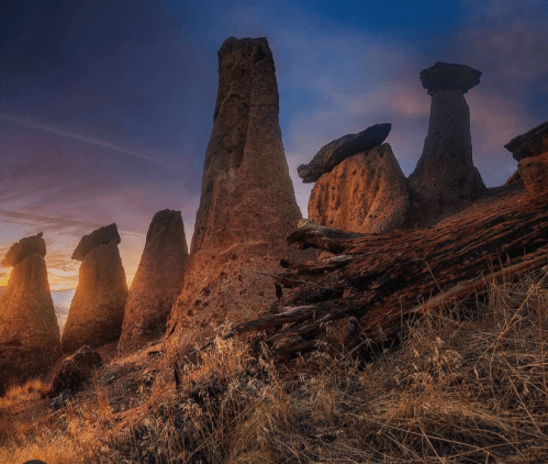 A dramatic landscape featuring towering rock formations at sunset, with golden grass in the foreground.