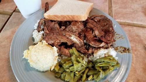 A plate of rice topped with seasoned meat, green beans, a scoop of mashed potatoes, and a slice of bread.