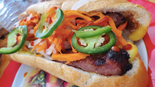 A close-up of a hot dog topped with sliced jalapeños, carrots, and onions in a soft bun.