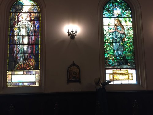 Stained glass windows depicting two figures, one angelic and one woman, in a church setting.