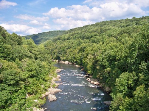 A serene river flows through lush green hills under a partly cloudy sky.