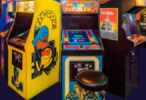Colorful vintage arcade machines featuring Pac-Man and Tetris, with a black stool in front.
