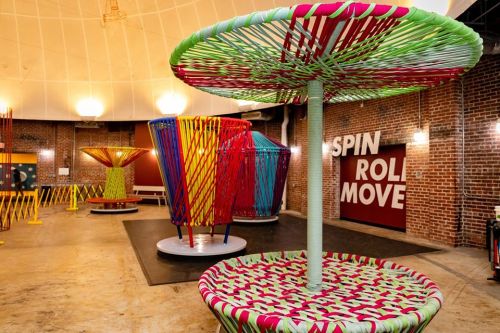 Colorful, large, circular sculptures made of woven materials in a spacious, industrial-style gallery.