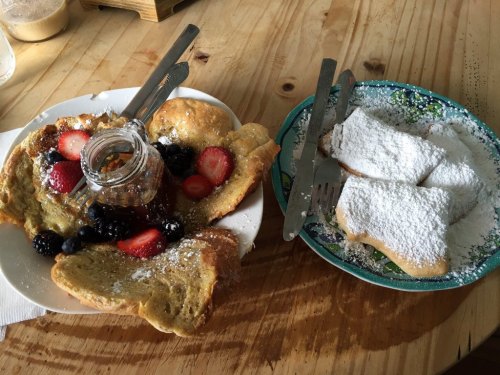 A plate of French toast topped with berries and syrup, alongside a plate of powdered sugar-dusted pastries.