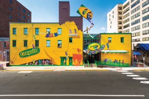 Brightly colored Crayola Experience building with playful murals and a large Crayola flag, located on a city street.