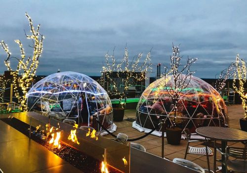 Two illuminated igloo-like structures on a rooftop, surrounded by twinkling lights and a fire feature in the foreground.