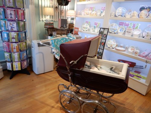 A vintage baby stroller in a shop, surrounded by decorative plates and greeting cards on display.