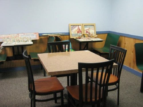 A small, empty room with a table and chairs, featuring framed artwork on the walls and a carpeted floor.