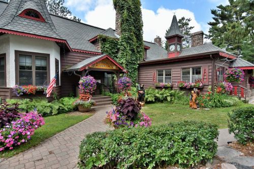 Charming lodge surrounded by vibrant flowers and greenery, featuring a clock tower and welcoming entrance.