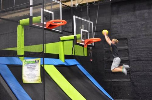 A person jumps to dunk a basketball at a trampoline park with two hoops.