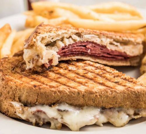 A close-up of a grilled sandwich with layers of meat and cheese, served with crispy French fries on the side.