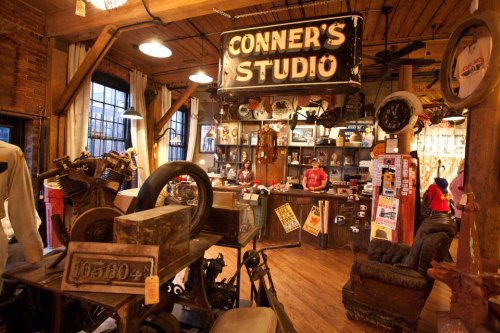 A vintage studio filled with eclectic decor, old machinery, and a large sign reading "CONNER'S STUDIO."