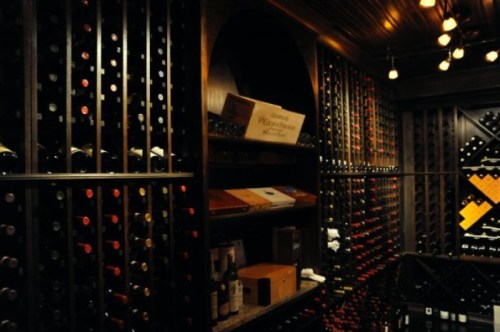 A dimly lit wine cellar with wooden racks filled with various wine bottles and a few boxes on the shelves.