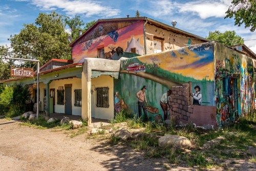 Colorful mural on a building with a sign reading "Theater," surrounded by greenery and rocky terrain.