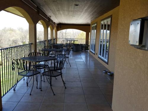 A covered patio with metal tables and chairs, overlooking a grassy area, with stacked chairs in the background.