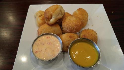 A plate of golden-brown bread rolls served with two dipping sauces: a creamy dip and a yellow mustard.