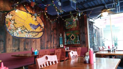 Cozy restaurant interior with wooden tables, colorful wall art, and festive decorations.