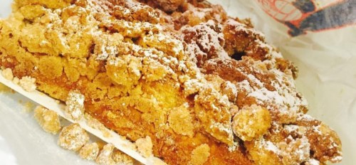 A close-up of a crumbly, powdered sugar-topped dessert, showcasing its golden-brown texture and layers.