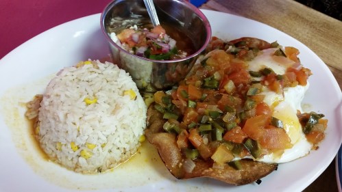 A plate of rice, a fried tortilla topped with eggs, tomatoes, and peppers, served with a small bowl of beans.
