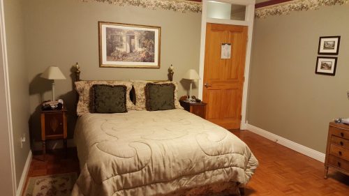 Cozy bedroom with a queen bed, decorative pillows, nightstands, and a wooden door, featuring floral wallpaper.