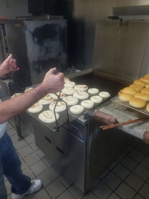 A person using tongs to flip bagels on a grill, with golden-brown bagels on a rack nearby.