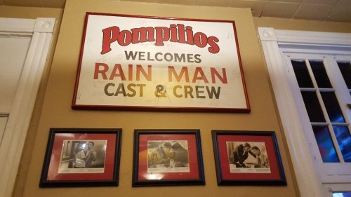 Sign reading "Pompilios Welcomes Rain Man Cast & Crew" with framed photos below it on a wall.