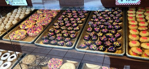 A display of colorful baked goods, including donuts and decorated cookies, in a bakery case.