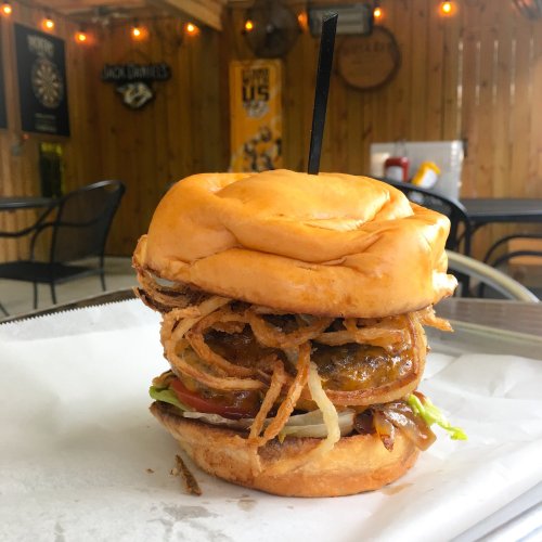 A stacked burger with crispy onion rings, lettuce, tomato, and sauce, served on a toasted bun.