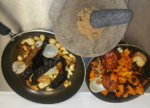 Two frying pans with sautéed garlic, onions, and chiles, alongside roasted chorizo and squash, with spices above.
