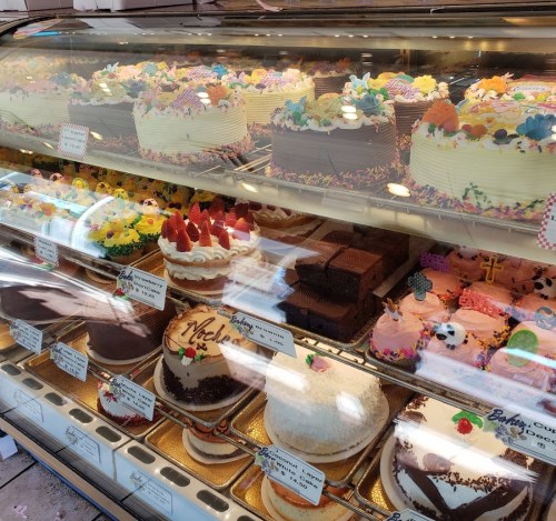 A display case filled with colorful cakes, decorated with flowers, sprinkles, and various toppings.