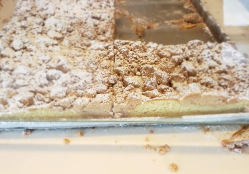 Close-up of a crumbly dessert topped with powdered sugar, partially cut and resting on a tray.