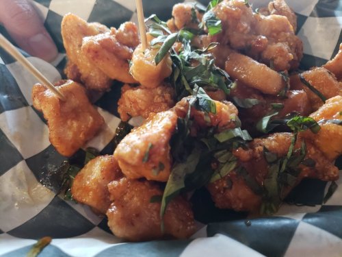 A close-up of crispy chicken pieces garnished with fresh basil, served on a checkered paper plate with skewers.