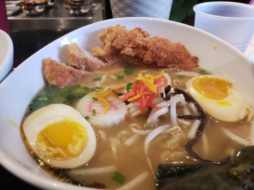 A bowl of ramen with crispy chicken, soft-boiled eggs, vegetables, and garnishes in a savory broth.