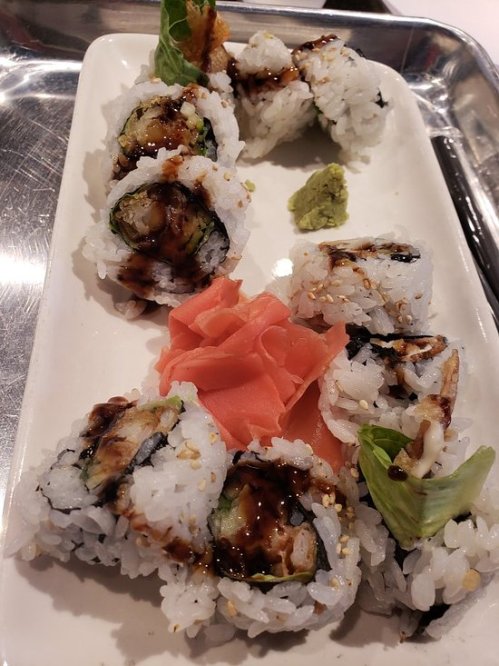 A plate of sushi rolls with eel, avocado, and cucumber, garnished with wasabi and pickled ginger.