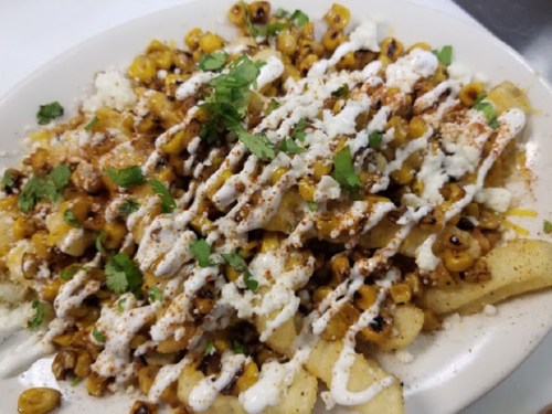 A plate of loaded fries topped with corn, cheese, drizzled sauce, and fresh herbs.