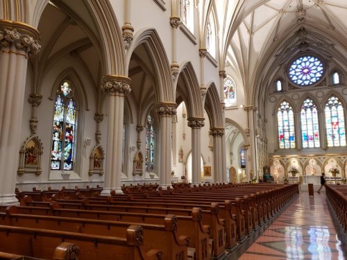 Interior of a grand church featuring tall arches, stained glass windows, and rows of wooden pews.