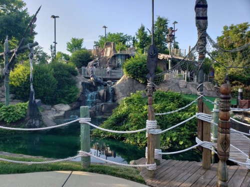 A scenic mini-golf course featuring a waterfall, lush greenery, and pirate-themed decorations.