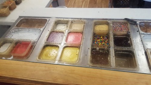 A display of various ice cream flavors and toppings in clear containers, including sprinkles and colorful candies.