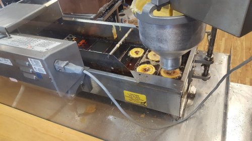 A deep fryer with a metal basket cooking food, surrounded by oil and kitchen equipment.